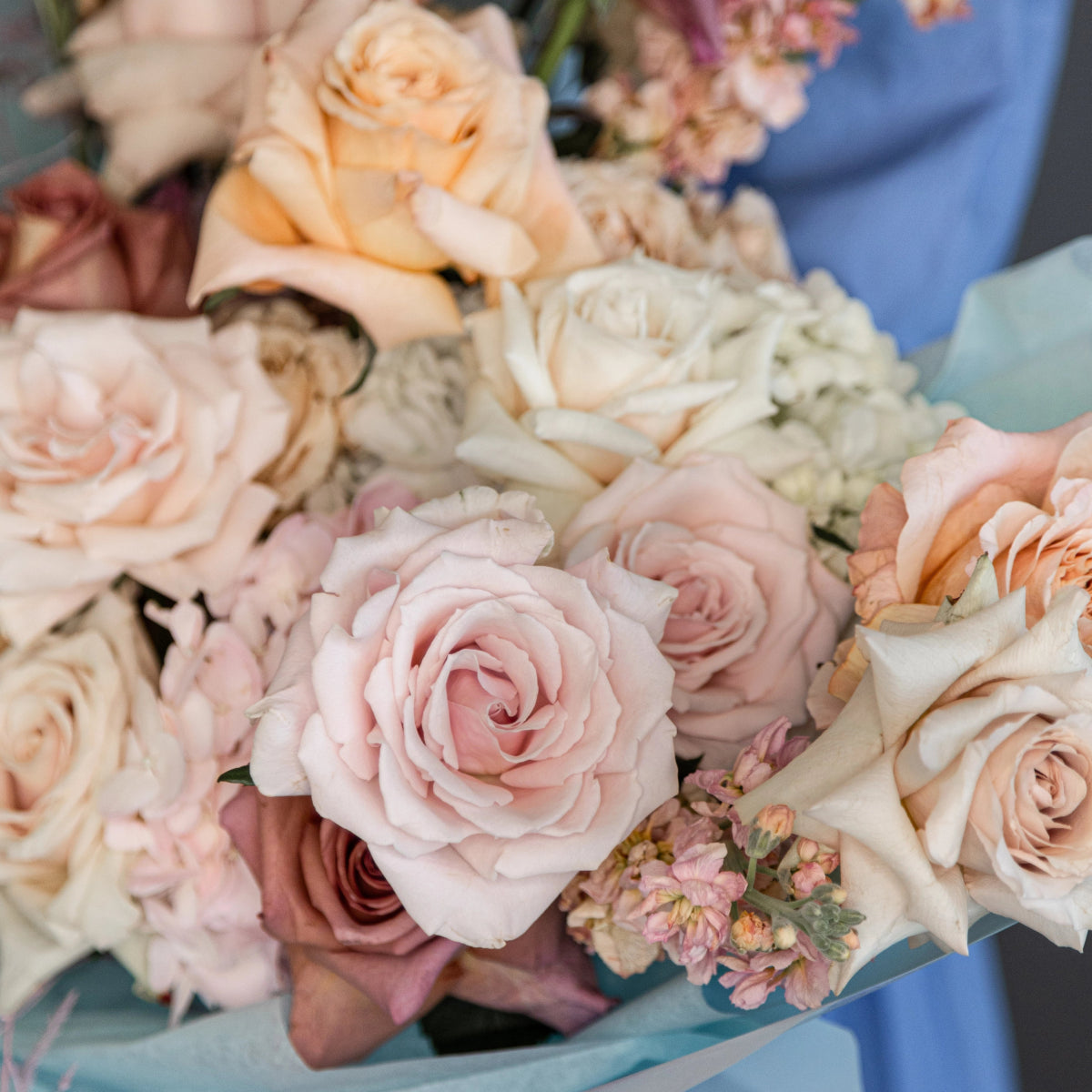 Pastel bridal bouquet with blush pink, peach and cream roses wrapped in blue ribbon