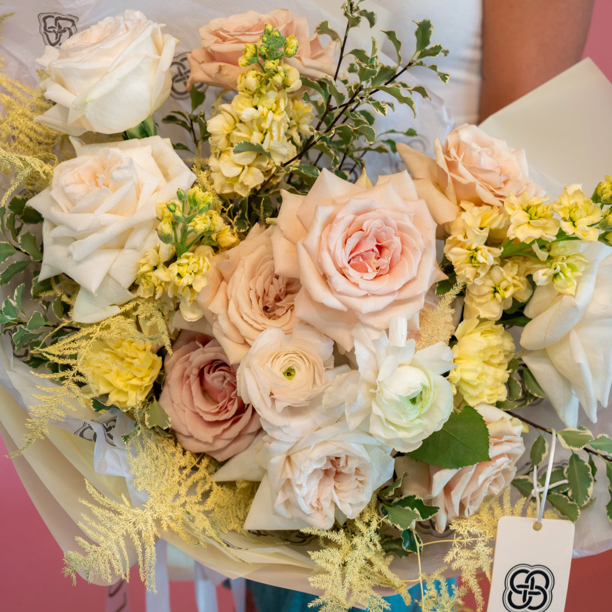 Pastel rose and ranunculus bouquet with yellow flowers and golden mimosa in cream paper wrapping