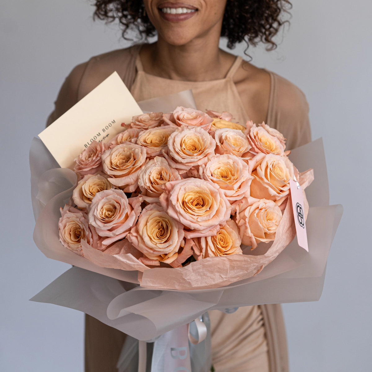 Elegant bouquet of peach and champagne roses wrapped in cream paper with satin ribbon held by smiling woman