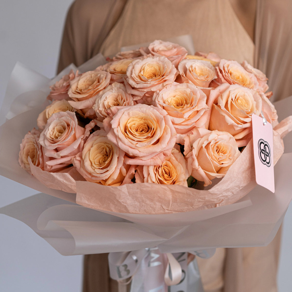 Elegant peach rose bouquet with white tissue paper wrapping and ribbon, perfect for gifting or special occasions