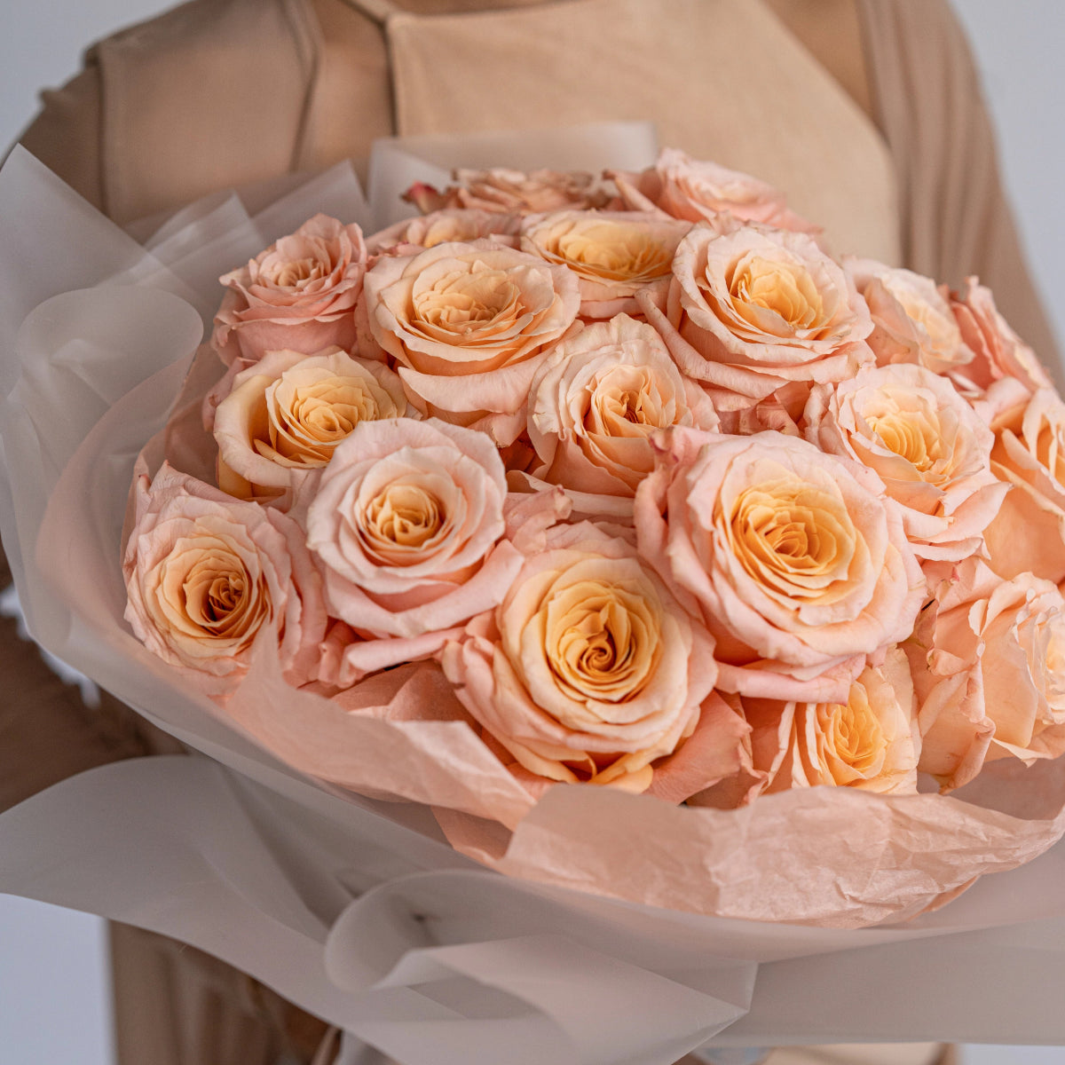 Elegant peach rose bouquet wrapped in soft white tissue paper with layered ruffled petals