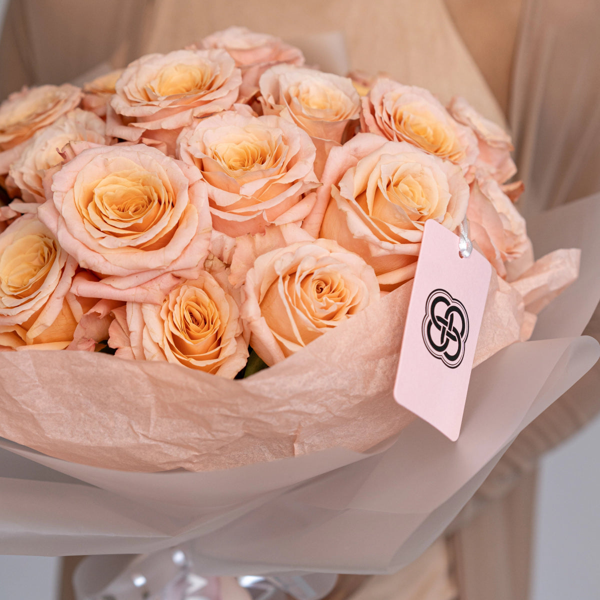 Elegant peach roses bouquet wrapped in soft pink tissue paper with branded gift tag on white surface