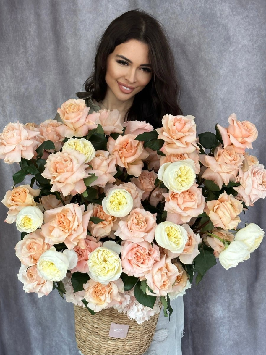 Luxury flower basket with peach and white roses, cream ranunculus in natural wicker basket with white ribbon