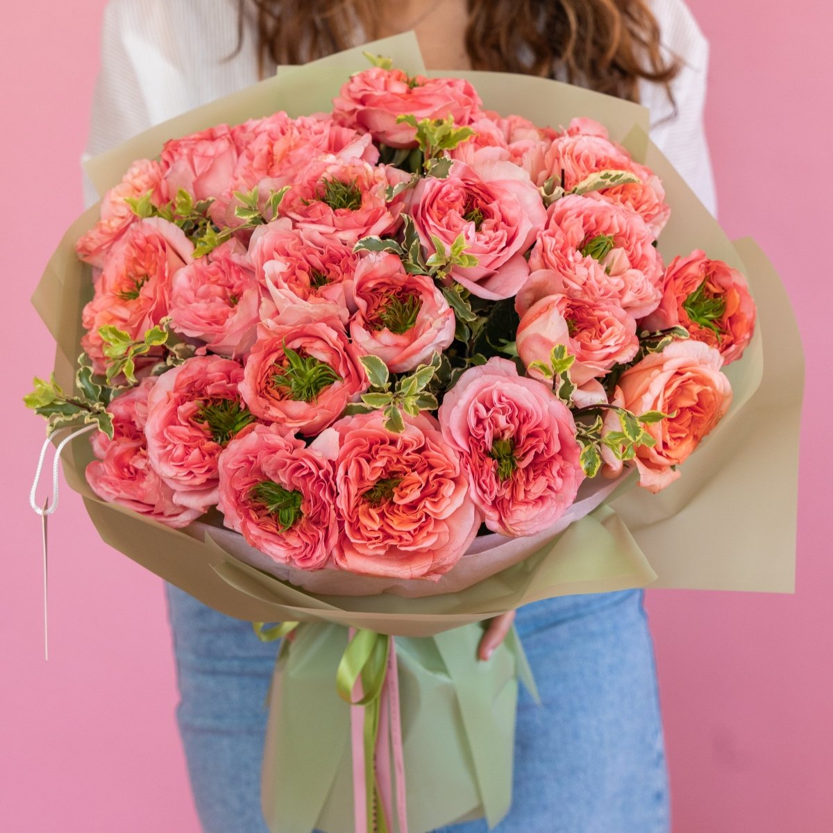 Pink coral garden roses bouquet with green foliage wrapped in sage green paper with ribbon ties