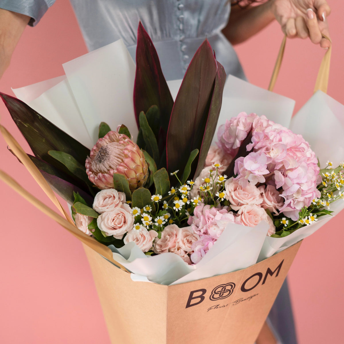 Pink rose and hydrangea bouquet with protea and chamomile daisies in white tissue paper gift wrapping