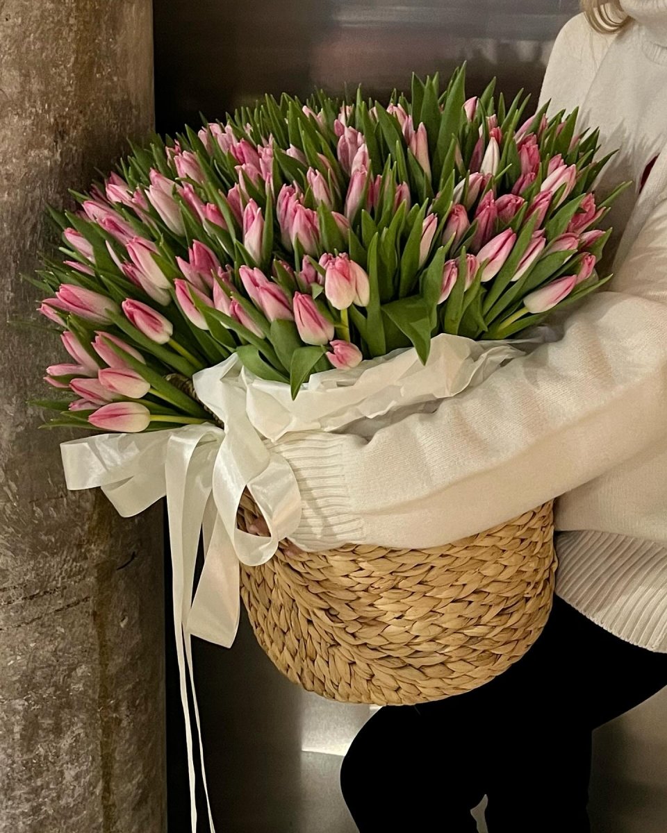Large wicker basket filled with pink and white tulip buds tied with cream ribbon bow