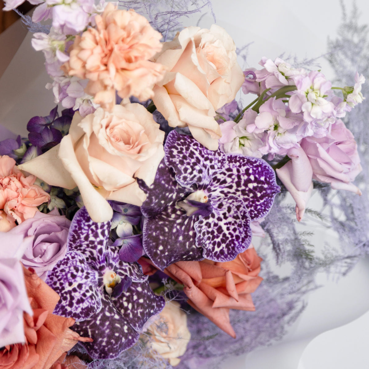 Purple spotted orchids with peach roses, coral carnations and lavender sweet peas in mixed floral bouquet
