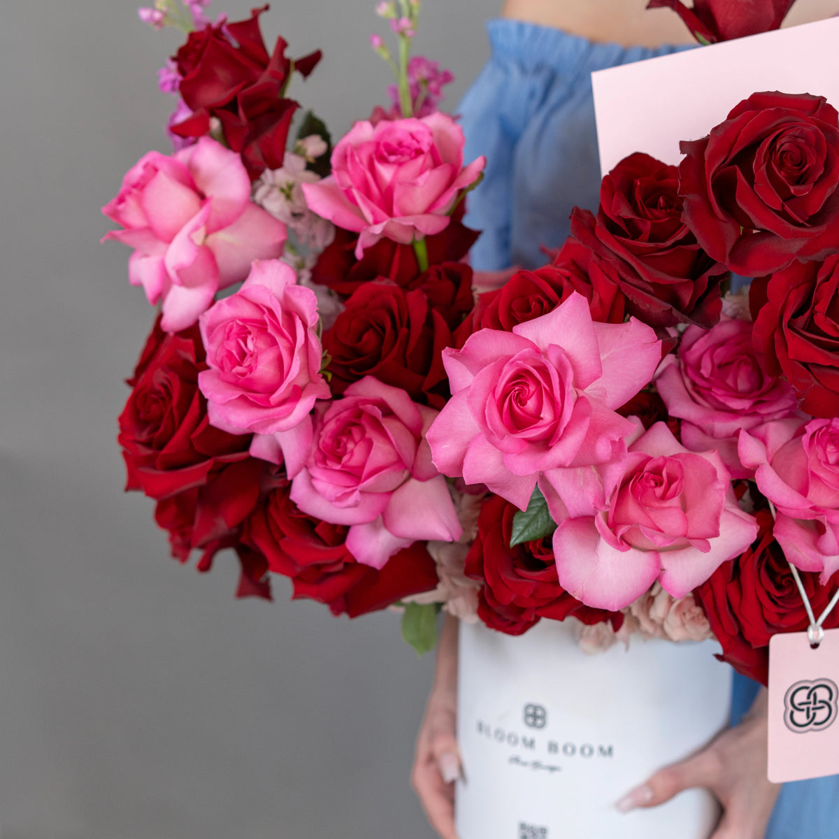 Elegant white flower box filled with deep red and pink roses, held by person in blue shirt with gift tag