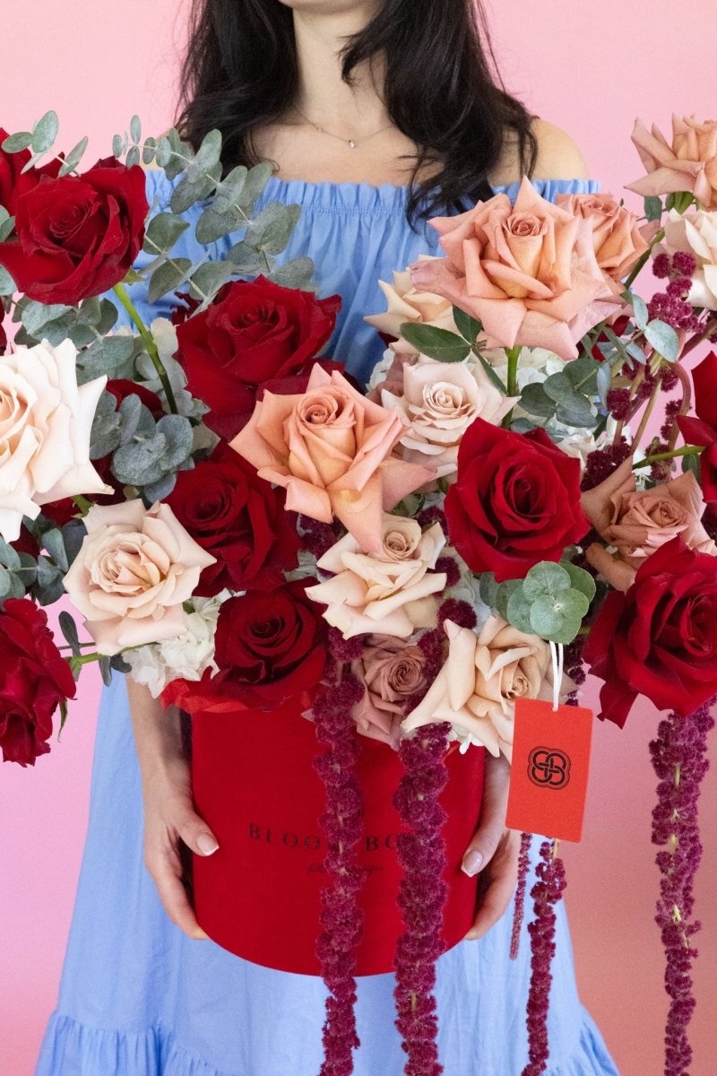 Red velvet flower box with mixed roses in burgundy, pink, and cream tones plus eucalyptus greenery