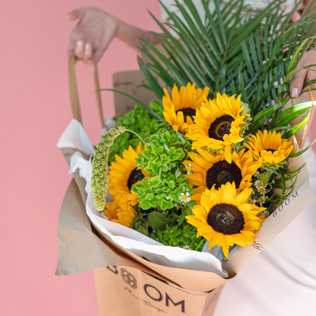 Bright yellow sunflower bouquet with green chrysanthemums and palm leaves in kraft paper wrapping