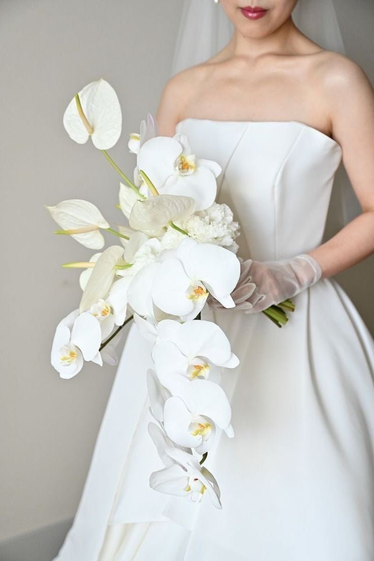 White orchid and anthurium cascading bridal bouquet with baby's breath held by bride in strapless gown