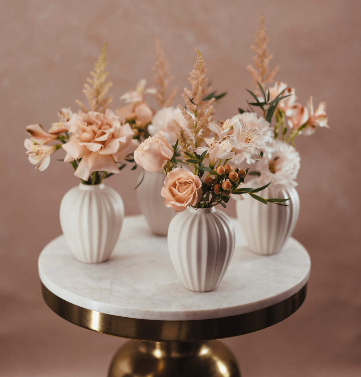 Three white ceramic ribbed vases with blush pink roses and dried grasses on marble gold-rimmed table