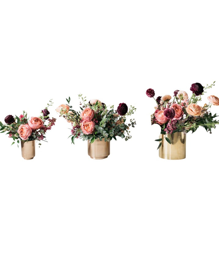 Three Bloom Boom arrangements side by side in brass vessels — Petite, Medium, and Deluxe — growing in size and fullness from left to right.